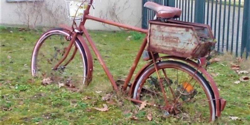 Ein altes Fahrrad steht zum Teil mit den Rädern verbuddelt auf einer Wiese.