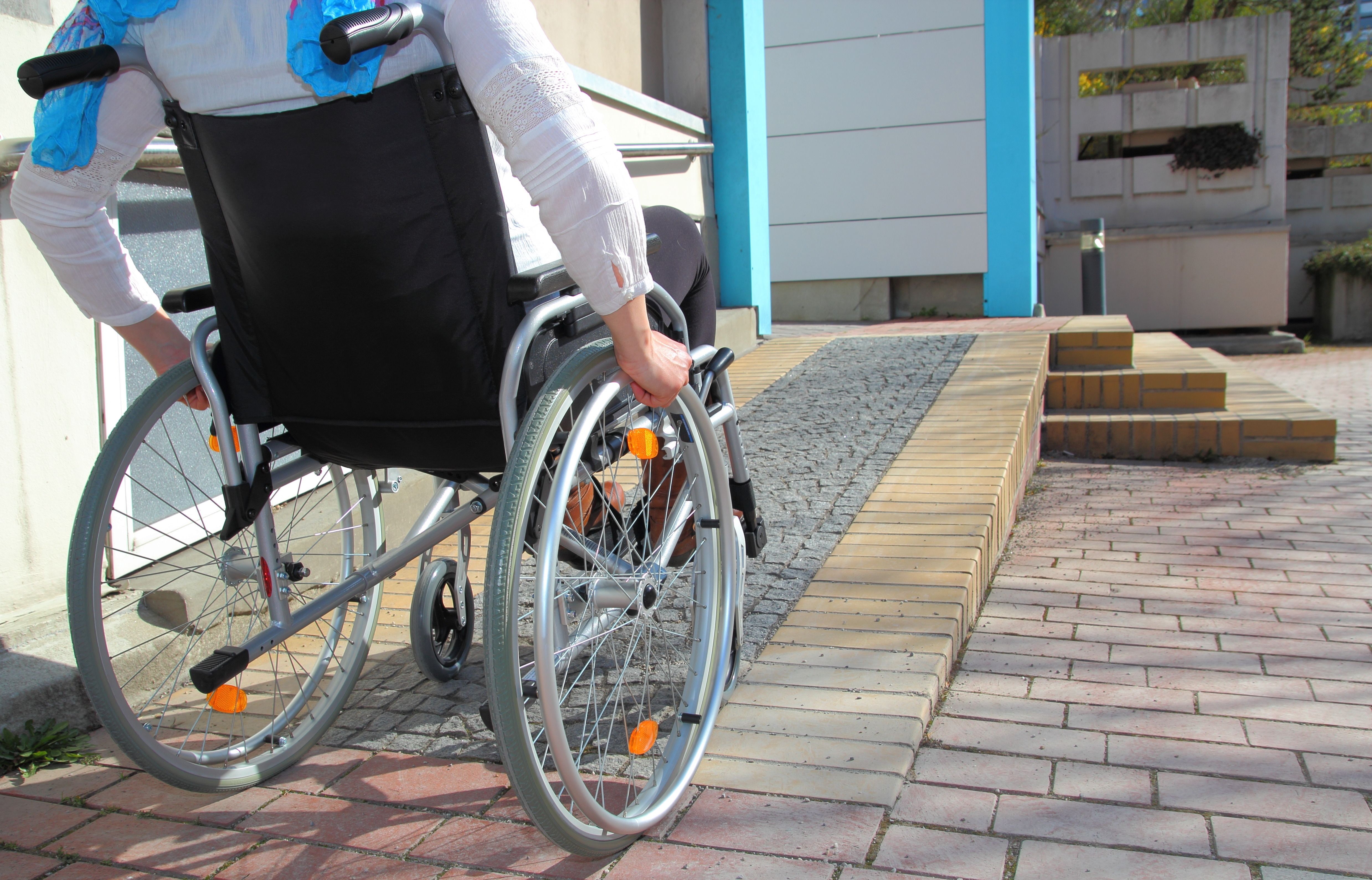 Person im Rollstuhl an einer rollstuhlgerechten Rampe, die zu einer Tür führt
