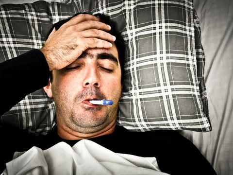 Mann mit Fiebertermometer im Mund liegt im Bett
