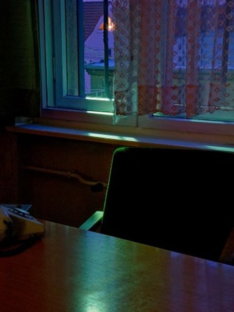 Bildvergrößerung: Hier sehen Sie ein Foto eines dunkeln Raumes, es scheint Licht herein, man sieht einen Tisch, einen Stuhl und ein Telefon