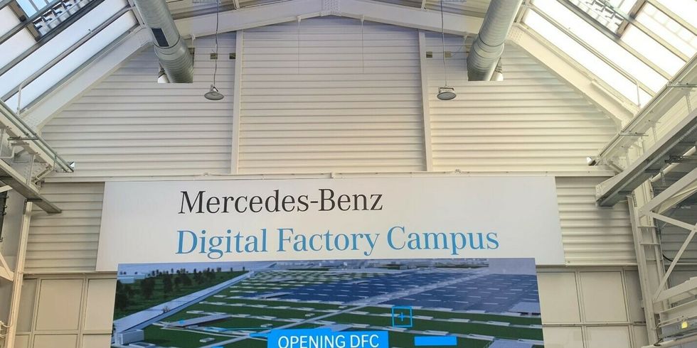 In einer großen Halle hängt an einem Ende an der Wand ein großes Schild mit der Aufschrift "Mercedes-Benz Digital Factory Campus".