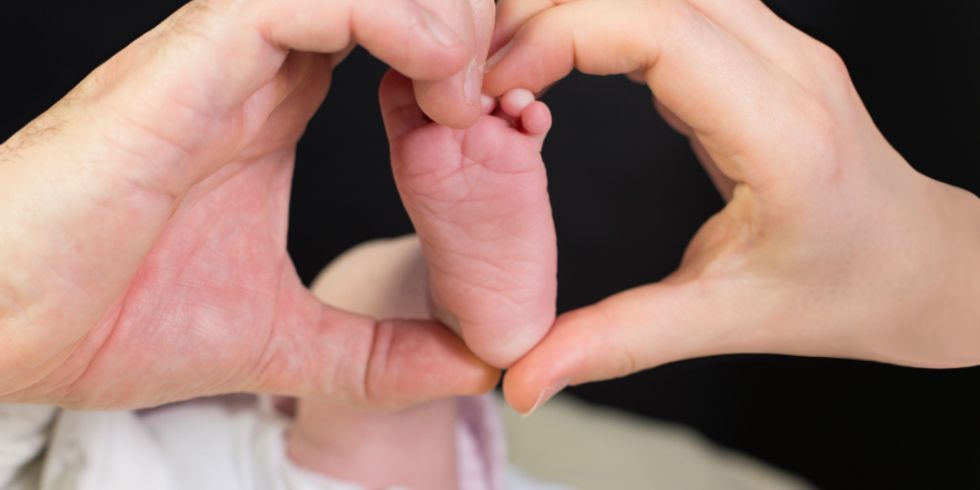 Zwei Hände formen ein Herz um den Fuß eines Säuglings
