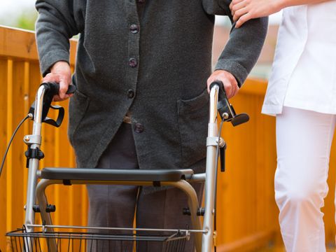Bildausschnitt Pflegerin stützt Senior mit Rollator auf Spaziergang
