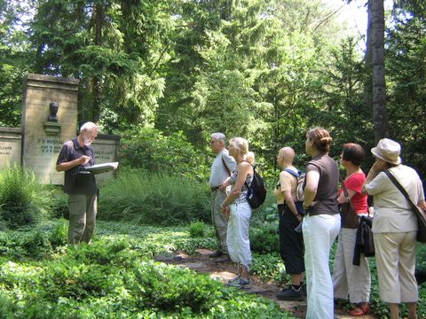 Der Exkursionsleiter steht vor einem Grabmal und eine Gruppe von Teilnehmern hört ihm zu.