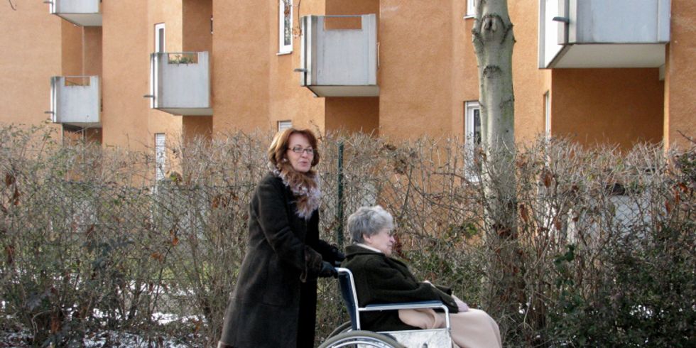 Eine Seniorin im Rollstuhl wird von einer Dame geschoben