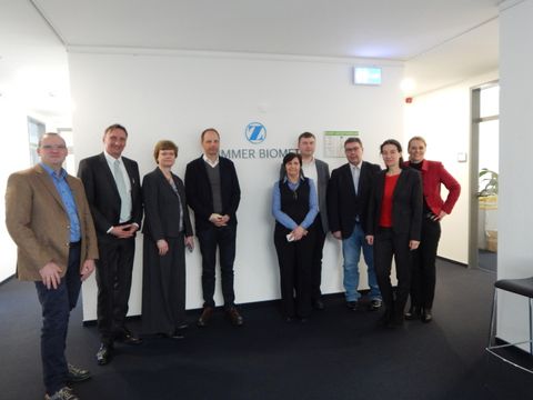Gruppenbild vor dem Zimmer-Biomet Logo mit Bezirksbürgermeisterin Cerstin Richter-Kotowski, Unternehmen Zimmer-Biomet, Wirtschaftsförderung Steglitz-Zehlendorf und Berlin Partner