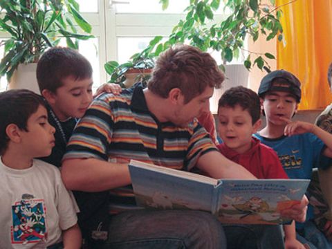 Ein Mann liest mit mehreren Kindern ein Buch