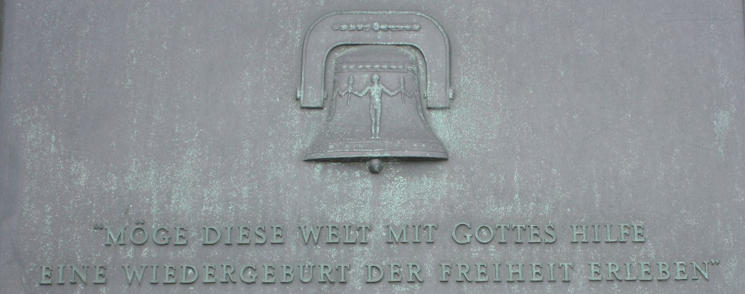 Das Relief einer Glocke mit dem Satz "Möge diese Welt mit Gottes Hilfe eine Wiedergeburt der Freiheit erleben" darunter