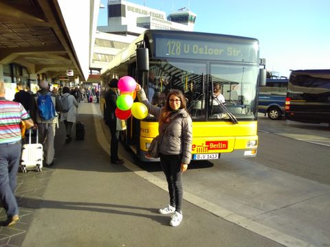 Eine junge Frau steht mit 5 Luftballons vor einem Linienbus