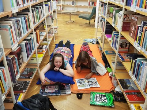 zwei Mädchen liegen auf Luftmatratzen zwischen Bücherregalen