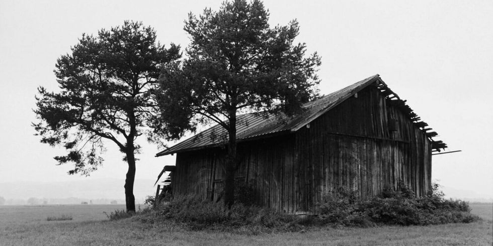 Eine schwarz-weiß Fotografie von einer alten Scheune auf einem Feld.