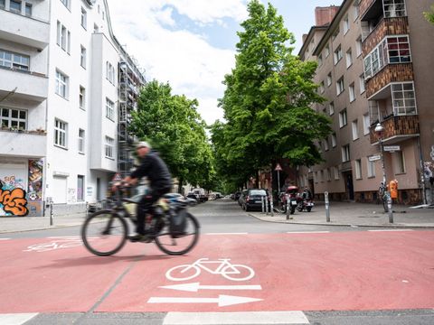 Bild von der Fahrradstraße im Schillerkiez mit schwarzem Radfahrer, Häuser und Bäume im Hintergrund