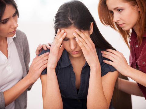 Depressive Frau sitzt am Lehrstuhl während zwei andere Frauen, die ihr beruhigend