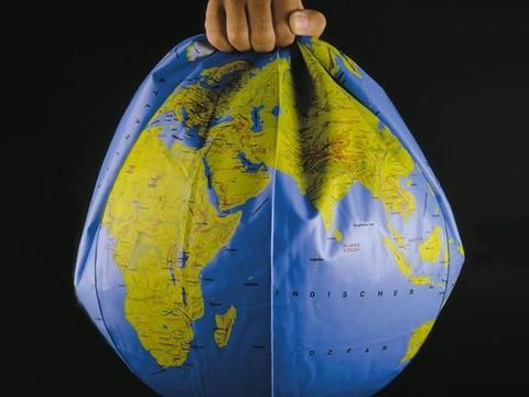 Globus in Form eines Wasserballs, dem etwas Luft fehlt, gehalten von einer Menschenhand am Nordpol