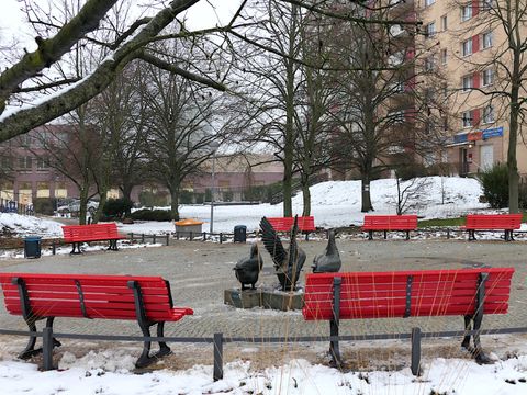 Runder Platz mit Gänseplastik und roten Bänken im Winter