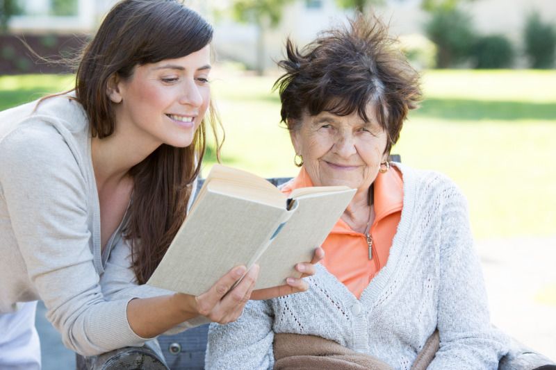 Junge Frau liest Senioren aus einem Buch vor