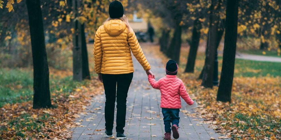 Frau geht mit kleinem Kind an der Hand im Herbst spazieren