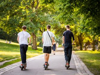 Drei Jungs fahren mit E-Scootern durch den Park