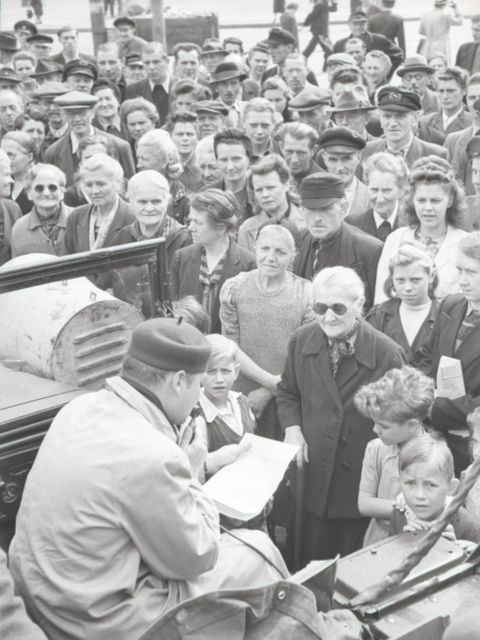 Enlarge photo: A crowd is facing a man in an open car, who is reading from a sheet of paper.