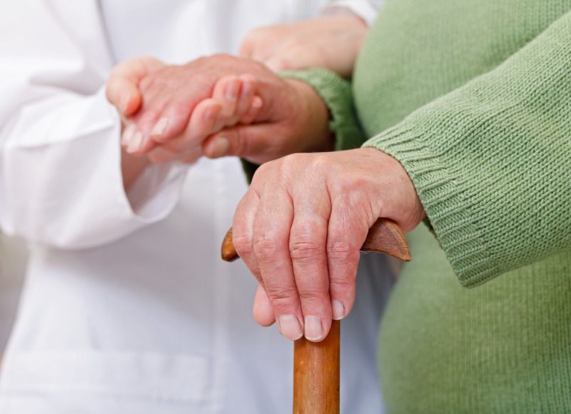 Bildausschnitt Arzt hält Hand von Seniorin mit Krückstock
