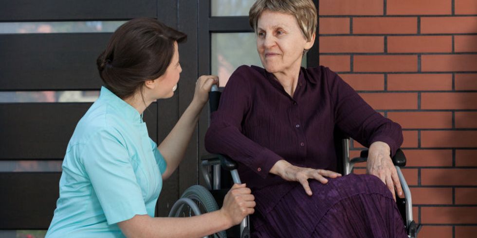 Pflegerin kniet neben einer Frau in einem Rollstuhl