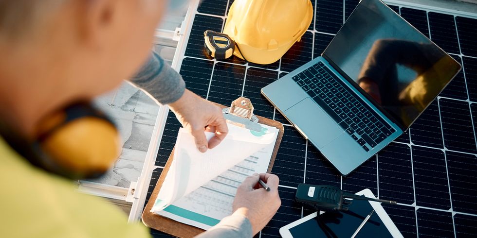 Person mit Unterlagen und Laptop vor einem Solarpanel