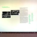 Bildvergrößerung: Eingangswand der Galerie mit einem einführenden Text und zwei historischen Fotos zum Thema der Ausstellung
