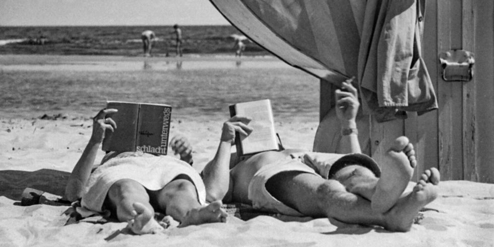 Altes Schwarz-Weiß-Foto mit zwei Menschen, die am Strand liegen und lesen.
