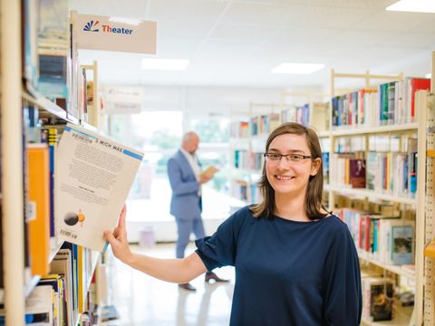 Junge Frau holt sich Buch aus einem Bücherregal in einer Bibliothek 