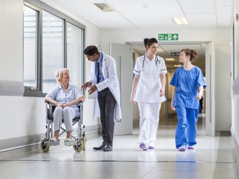 Krankenhausflur mit medizinischem Personal und Patientin im Rollstuhl