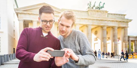 Zwei Männer schauen auf Smartphone, im Hintergrund Brandenburger Tor