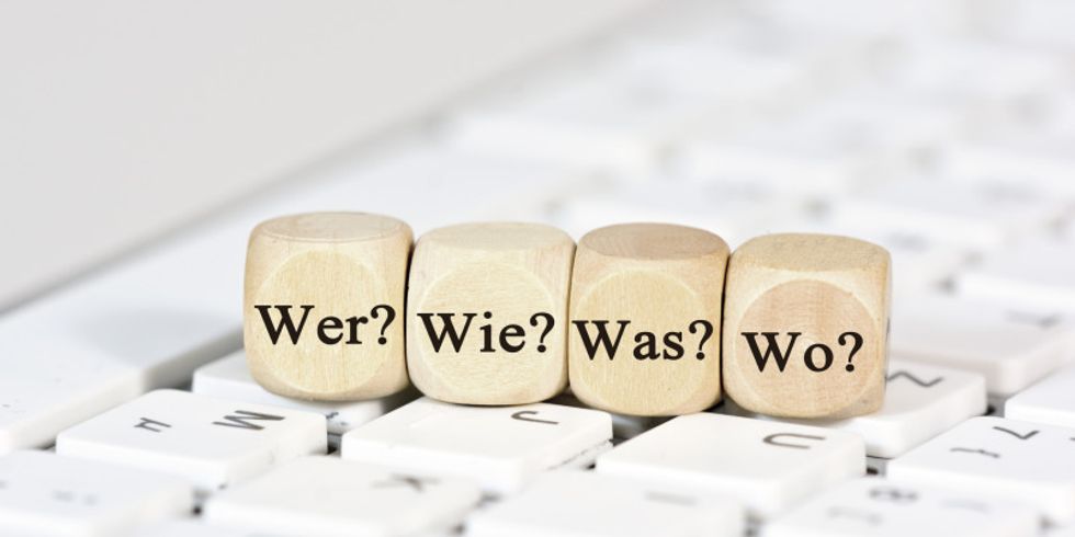 Auf einer Tastatur liegen vier Würfel mit den Aufschriften 'Wer?', 'Wie?', 'Was?', 'Wo?'