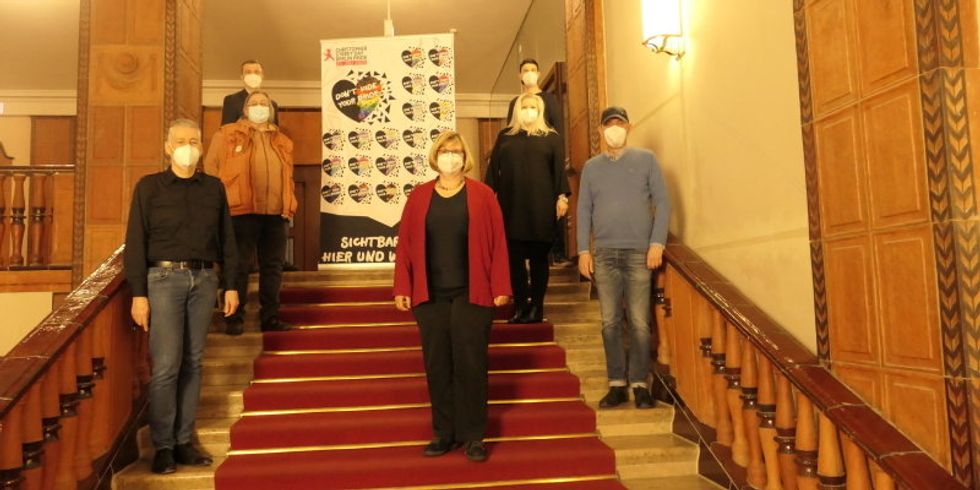Zei Frauen und fünf Männer stehen auf einer Treppe vor einem Banner des Christopher Street Day