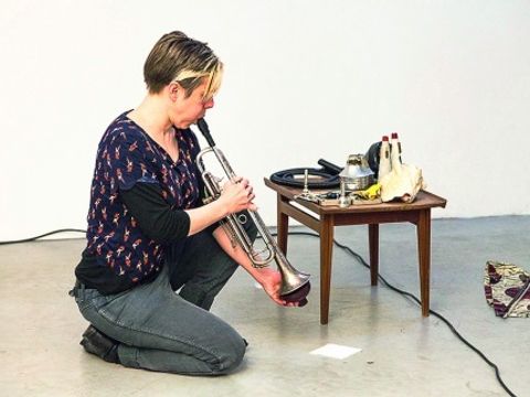Bildvergrößerung: Hier sehen Sie eine Frau, die auf dem Boden sitzend Trompete spielt