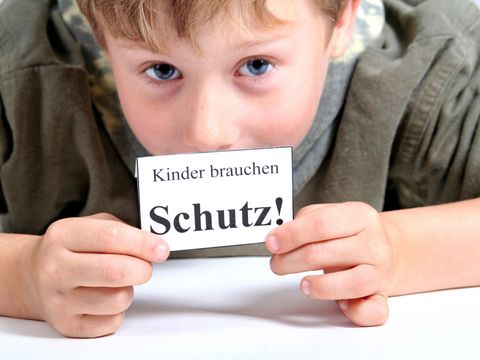 Junge hält Zettel mit Aufschrift: Kinder brauchen Schutz
