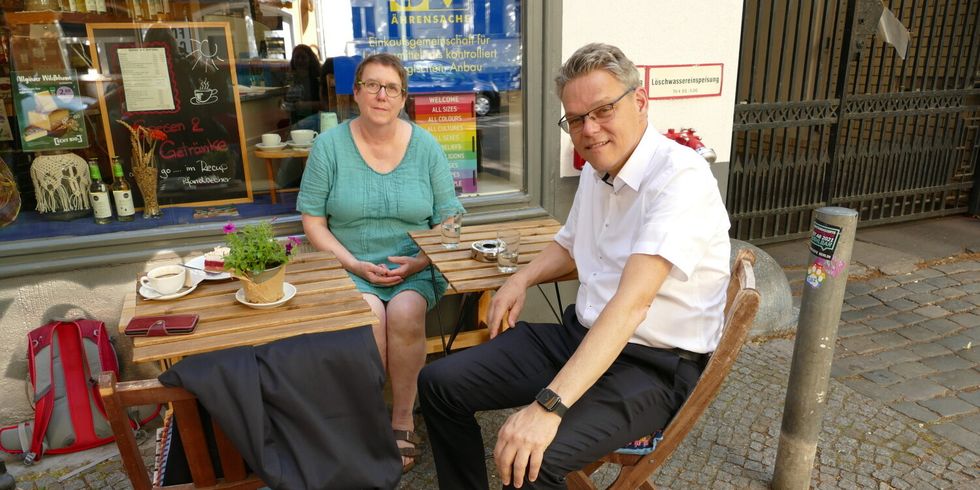 Ein Mann und eine Frau sitzen zusammen an Tischen vor einem Geschäft.