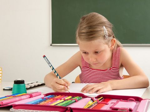 Mädchen sitzt im Unterricht und schreibt mit Bleistift 