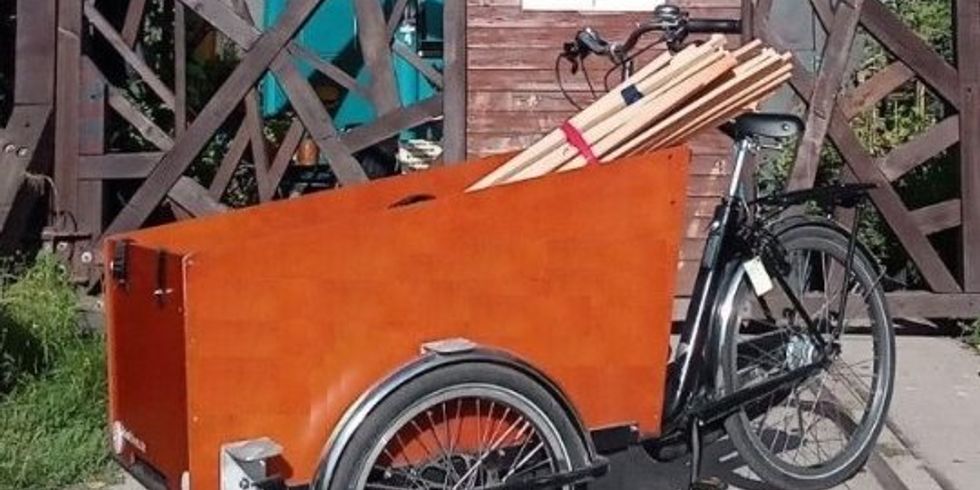 Ein Lastenrad mit Holzlatten beladen steht vor einem Holztor.
