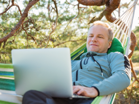 Mann mit einem Laptop in einer Hängematte mitten im Wald