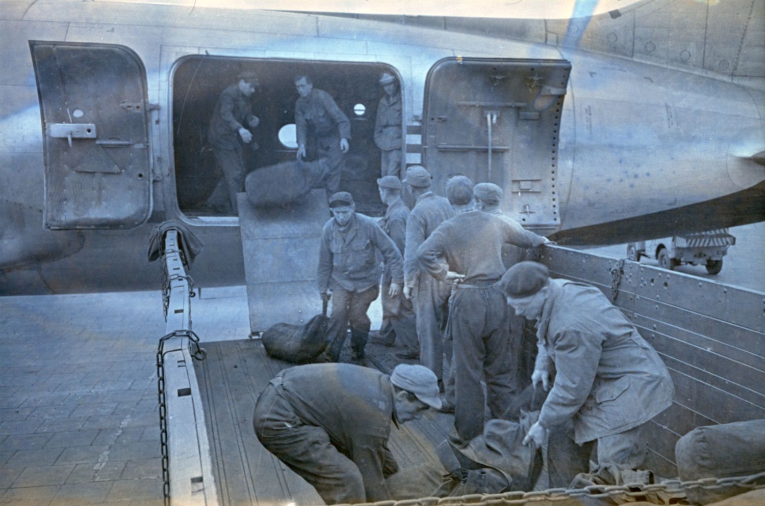 Enlarge photo: Men are unloading cargo bags from an airplane.