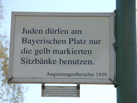 Ein schild an einem Laternenmast auf dem steht: "Juden dürfen am Bayerischen Platz nur die gelb markierten Sitzbänke benutzen"
