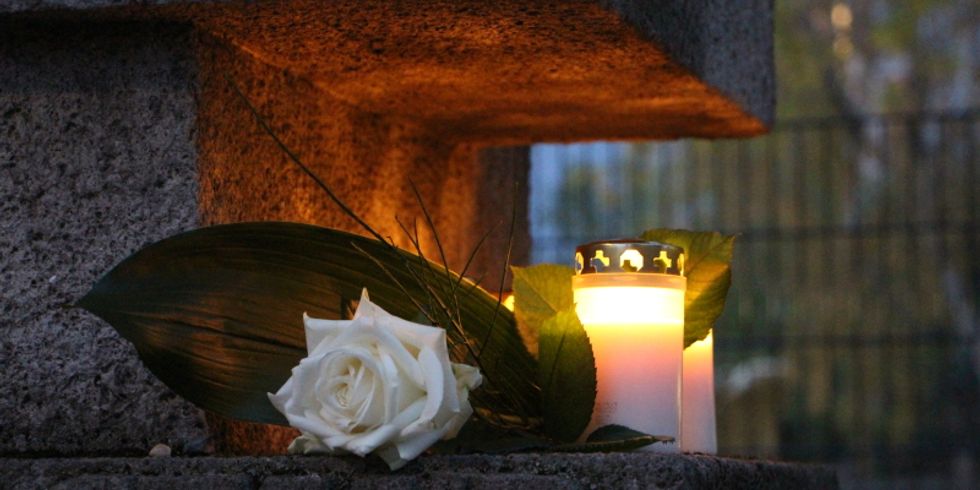 Weiße Rose mit Kerzen auf einem Gedenkstein