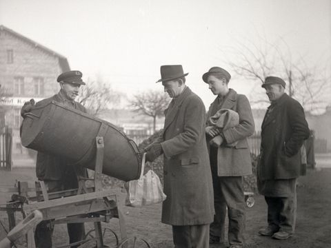 Enlarge photo: Three men are waiting in line for the distribution of goods by another man.