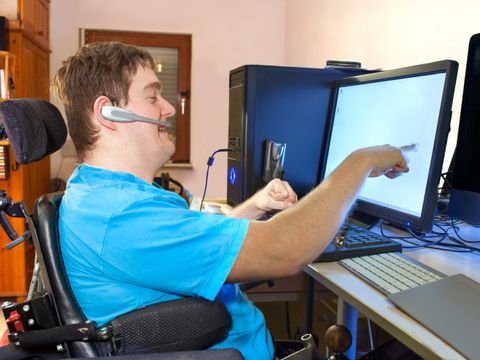 Mann im Pflegerollstuhl sitzt am Computer