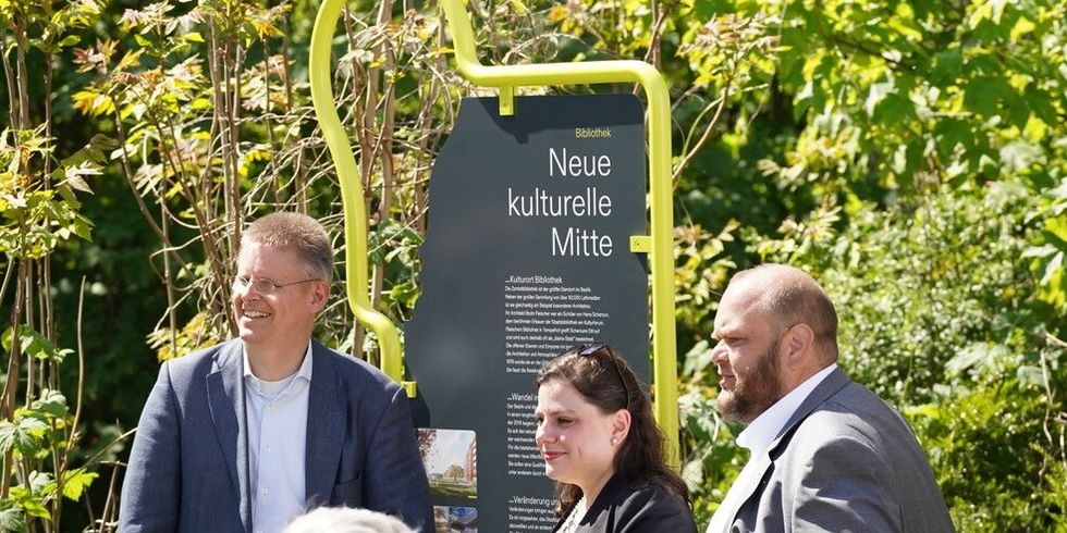Drei Personen stehen vor einem Schild mit der Aufschrift "Neue kulturelle Mitte"