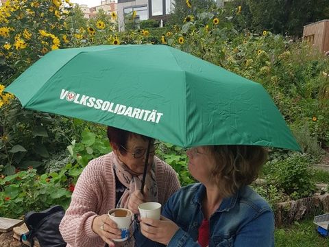 zwei Frauen trinken Kaffee im Garten unter einem Regenschirm