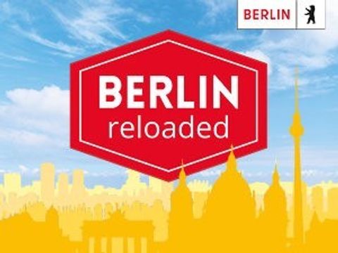 Ein Schild in dem der Text Berlin reloaded steht vor verschiedenen Gebäuden aus Berlin.