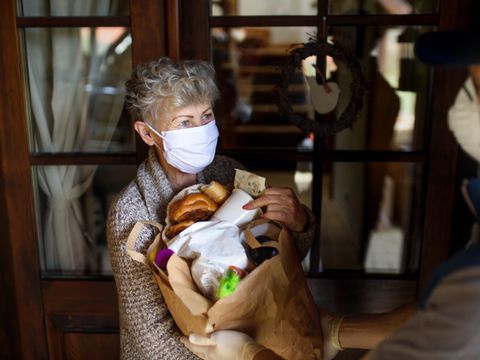 Kurier bringt Seniorin mit Mundschutz Einkäufe