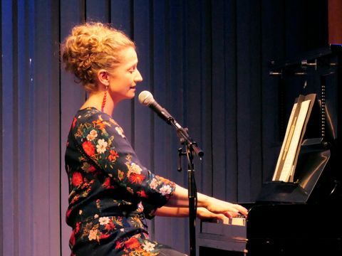 Ein Frau spielt Klavier und singt dabei in ein Mikrofon.