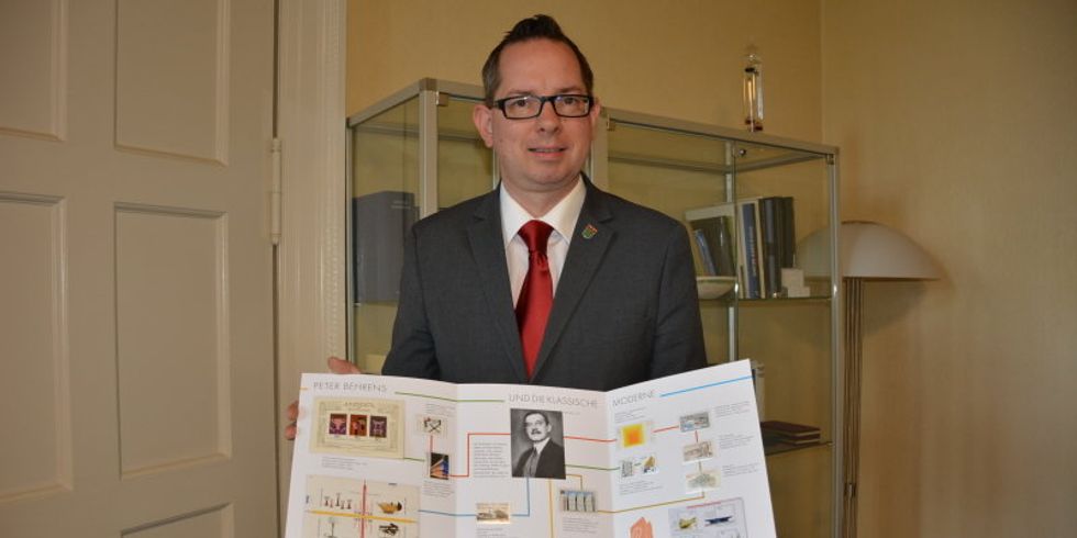 Bezirksbürgermeister Oliver Igel präsentiert das Gedenkset zur Sonderbriefmarke Peter Behrens